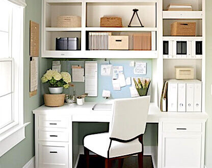A home office nook with white shelves, , white desk, dark wood and white upholstered chair, cream rug, rope bins and office supplies.